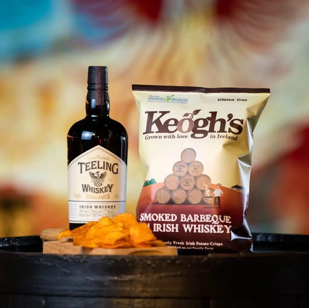 Teeling X Keoghs crisps. A bottle of Teeling Whiskey Small Batch with a bag of Keoghs crips and some on the side.