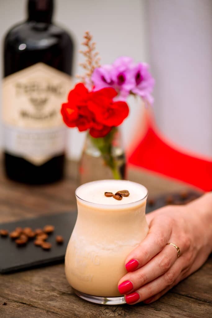 Close up of Teeling Frozen Irish coffee hand by woman's hand. Teeling Small Batch in background